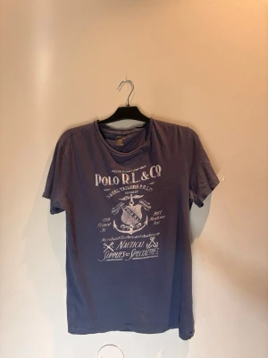 Mörkblå t-shirt från Polo RL & Co - Snygg mörkblå t-shirt från Polo RL & Co med stort tryck framtill i vitt med nautiskt tema. Klassisk rund hals och korta ärmar. Perfekt för dig som gillar en avslappnad och stilren look.