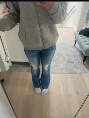 Blå lågmidjade slitna bootcut jeans - Säljer ett par blå bootcut jeans med slitningar på låren och knäna och fina fickor. Jeansen är använda max 3ggr då dem blev försmå. Men väldigt snygga