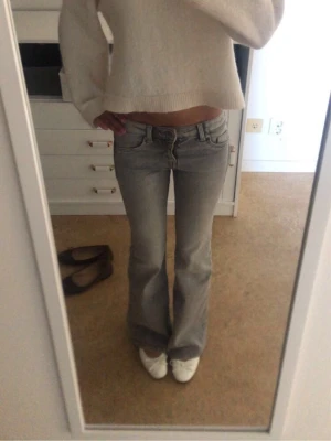 Ljusgrå bootcut jeans - Säljer ett par ljusgrå bootcut jeans med låg midja och klassiska fem fickor. Jeansen har en snygg tvättad look och är i ett mjukt denimtyg som sitter skönt. 😇