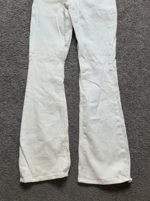 Vita bootcut jeans från Atlas - Snygga vita bootcut jeans från Atlas med klassisk femficksdesign och bälteshällor. Jeansen har en rak passform upptill och utsvängda ben, vilket ger en retrovibe. Tillverkade i ett mjukt och slitstarkt denimtyg som passar perfekt till många olika stilar.