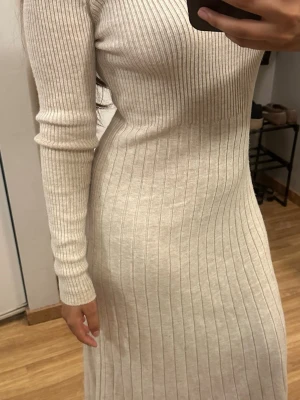 Ribbad långklänning med polokrage - Säljer en superfin långklänning i ljusbeige ribbad stickad kvalitet. Klänningen har lång ärm, hög krage och sitter figurnära för en snygg siluett. Perfekt för dig som gillar stilrena och bekväma plagg med en modern touch.