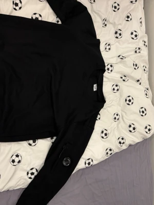 Svart sweatshirt med ficka på ärmen - En stilren svart sweatshirt med rund hals och lång ärm. Tröjan har en praktisk ficka med dragkedja och detalj på ena ärmen. Perfekt för en avslappnad och trendig look. Passar till det mesta och är enkel att matcha. Cp company 