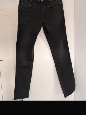 Svarta Replay jeans Ambass 33 - Säljer ett par svarta Replay Ambass jeans i storlek 33. Jeansen har en klassisk femficksmodell, raka ben och snygga slitningar för en cool look. Materialet är mjukt och stretchigt för extra komfort. Perfekta till sneakers eller boots.