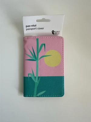 Rosa passfodral med grafiskt motiv - helt NYTT - Helt nytt passfodral från Flying Tiger i rosa med grafiskt tryck av en grön växt och en gul sol mot rosa och turkos bakgrund. Fodralet är gjort i ett tåligt syntetmaterial och har plats för ett pass. Perfekt för att hålla koll på passet under resan och för att se till att det håller sig helt och rent. 10x15cm. Helt nytt med etikett!