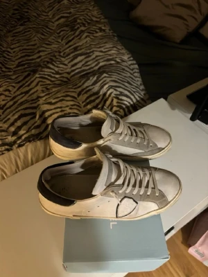 Phillipe model - Snygga vita sneakers från phillipe model med blå häl och gråa detaljer på sidan. Skorna har klassisk låg modell med vita snören och sula. Materialet ser ut att vara en mix av läder och mocka. Perfekta för en stilren och avslappnad look.