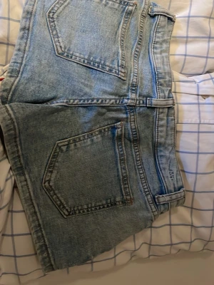 Ljusblå jeansshorts med dragkedja - Snygga ljusblå jeansshorts i klassisk denim med fem fickor, bälteshällor och dragkedja framtill. Perfekta för varma dagar och enkel att matcha med allt. Avslappnad passform och tidlös stil.