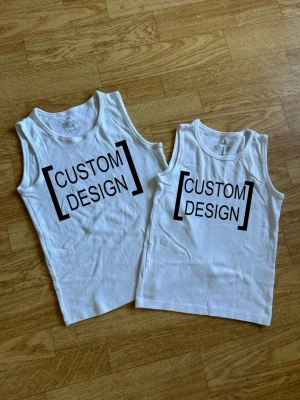 Vitt linne med egengjord design - Vid köp skapar jag en tröja med en (enkel) design som du väljer. Det kan vara ett ord, en fras, en logotyp, ett namn eller liknande. Det enda kravet är att motivet är relativt enkelt att utföra (exempel finns med). Tröjorna finns i barnstorlekar (122/128 och 134/140), men de kan även passa som XS/S (bild på hur storlek 134/140 sitter på mig finns med). Färgerna jag har är svart, vit, lila, grön och gul. Kan maskintvättas i 40 °C.