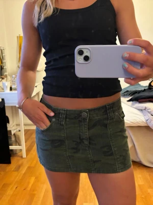 Slutsåld kjol från Nelly - Snygg grön kortkjol med camouflage-mönster och klassiska jeansdetaljer som fickor och bälteshällor. Kjolen har knapp och dragkedja framtill och är perfekt för dig som vill ha en cool och avslappnad stil. Slutsåld på Nelly. Använd en gång.