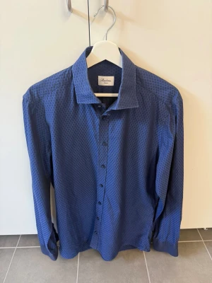 Blå skjorta från Stenströms, stl 41 - Snygg blå skjorta från Stenströms med diskret prickigt mönster. Skjortan har klassisk krage, knäppning framtill och långa ärmar. Perfekt för dig som vill ha en stilren look med lite extra detalj.