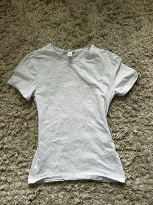 Vit basic t-shirt i bomull XS - En enkel och stilren vit t-shirt i mjuk bomull. Modellen är figurnära med korta ärmar och rund halsringning. Perfekt att matcha med jeans eller kjol för en clean look.