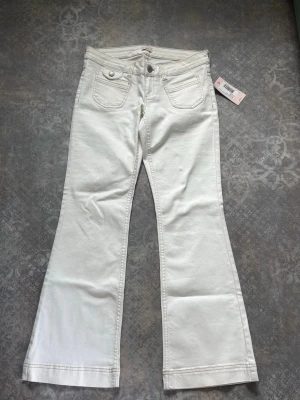 Vita bootcut jeans med fickor - Snygga vita jeans med bootcut-modell och klassiska fem fickor. Jeansen har vida ben och markerade sömmar, perfekta för en trendig och avslappnad stil. Tillverkade i ett mjukt denimtyg som ger en bekväm känsla hela dagen.