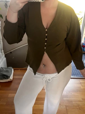Olivgrön cardigan med knappar - Den är liten i storleken! Snygg olivgrön cardigan med v-ringning och dekorativa knappar framtill. Tröjan har trekvartsärmar och en unik skärning nedtill som ger en cool look. Tillverkad i mjukt, stretchigt material som sitter skönt på kroppen.