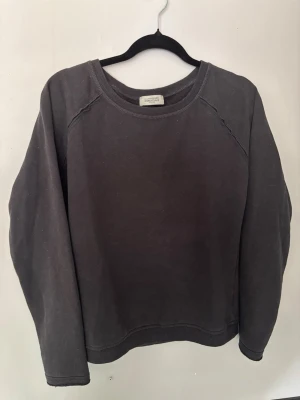 Svart Hunkydory sweatshirt med vingar - Cool svart sweatshirt med rund hals och långa ärmar. På ryggen finns ett stort tryck av vita änglavingar som ger tröjan en unik och edgy look. Perfekt för dig som vill sticka ut lite extra. Tillverkad i mjukt bomullsmaterial.