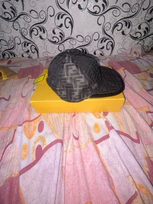 Svart keps med Fendi-logga - Säljer en svart keps från Fendi med det klassiska FF-mönstret över hela kepsen. Skärmen är i svart och har en snygg kontrast mot tyget. Perfekt accessoar för dig som vill ha en exklusiv och trendig look.