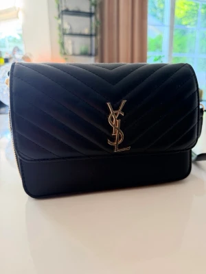 YSL axelväska  - Snygg svart YSL väska med guldfärgade detaljer och justerbar axelrem. 