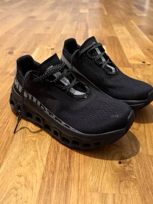 Svarta On Cloudmonster sneakers - Svarta On Cloudmonster sneakers med chunky sula och ventilerande mesh-ovandel. Skorna har reflekterande detaljer, svarta och vita snören samt logga på hälen. Perfekta för dig som gillar sportig och modern stil.