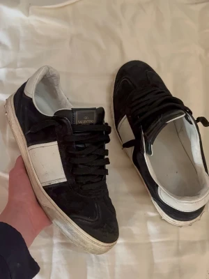 Valentino flycrew  - Snygga svarta sneakers från Valentino med vita detaljer och svart snörning. Skorna har en låg silhuett och är tillverkade i mocka och läder. Den vita panelen på sidan och den vita sulan ger en stilren kontrast till det svarta.