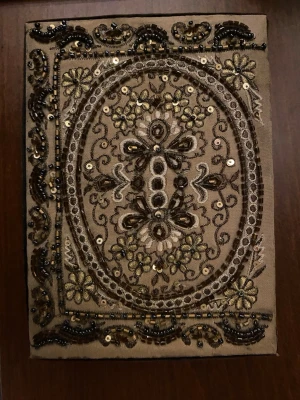 Brun dekorativ ask med pärlor - Säljer en unik brun ask med broderade detaljer och pärlor i guld och svart. Locket har ett blommigt mönster med paljetter och pärlor som ger en lyxig känsla. Asken är klädd i tyg både in- och utvändigt och passar perfekt för smycken eller småaccessoarer.
