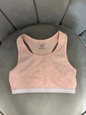 Ljusrosa sport-bh från OVS - En ljusrosa sport-bh från OVS med bred resår i vitt och rosa längst ner. Bh:n har brottarrygg och är tillverkad i mjukt bomullsmaterial, perfekt för dig som vill ha något bekvämt och enkelt under tröjan.