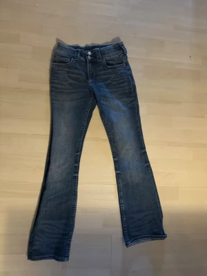 Blå bootcut jeans med slitningar - Säljer ett par blå bootcut jeans med lätt slitna detaljer och klassisk femficksdesign. Jeansen har normal midja och är tillverkade i denim med en snygg tvätt. Perfekta för en avslappnad och trendig look. storlek 158