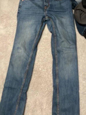Blå raka jeans från 157 - Säljer ett par klassiska blå jeans från 157 med rak passform och normal midja. Jeansen har fem fickor, gylf med knapp och dragkedja samt kontrastsömmar. Perfekta till vardags för en avslappnad stil.