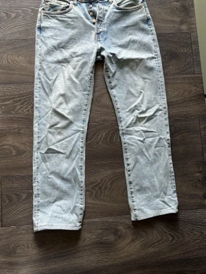 Ljusblå raka jeans med knappar - Säljer ett par ljusblå jeans med raka ben och knappgylf. Klassisk femficksmodell i denim med kontrastsömmar. Perfekta för en avslappnad och trendig look.