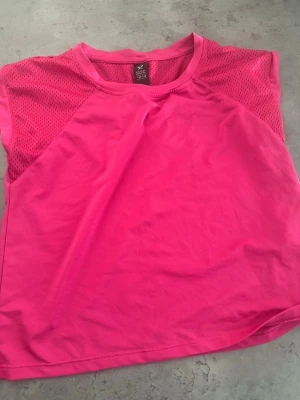 Rosa träningstopp från SOC. - Snygg rosa träningstopp från SOC med meshdetaljer på axlarna för extra ventilation. Toppen är ärmlös och har en sportig look, perfekt för aktiva dagar. Tillverkad i ett lätt och syntetiskt material som andas.