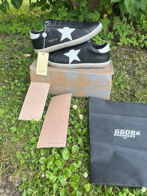Svarta Golden Goose sneakers med vit stjärna - Helt nya och HELT OANVÄNDA!🔥Helt oanvända med taggar kvar.‼️ Säljs till ett lågt pris för snabb affär.‼️Svarta sneakers från Golden Goose med vit stjärndetalj på sidan och vit häl. Skorna har svarta skosnören och en beige sula. Tillverkade i läder och levereras med originalkartong och tillbehör. Perfekta för en trendig och avslappnad stil.