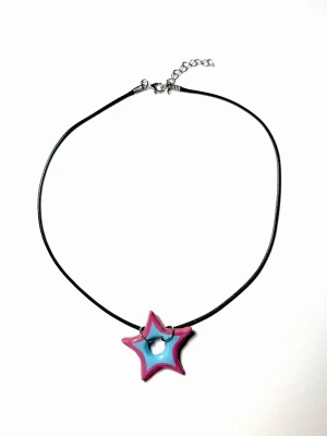 Halsband med stjärnhänge i blått och rosa - Handgjort halsband med svart snöre och ett stjärnformat hänge i blått och rosa som är tillverkat av lera. 