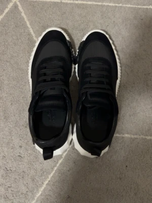 Svarta sneakers med vit sula - Snygga svarta sneakers med ribbad vit sula och svarta detaljer. Ovandelen är i textil och mockaimitation med klassisk snörning. Skorna har en modern, sportig look och passar perfekt till streetwear-stilen.