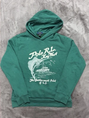 Grön hoodie Polo Ralph Lauren key west - Grön hoodie från Polo Ralph Lauren med vit tryckt 'Polo R.L. Key West'. Storlek XL barn passar M. Jag är 187 och väger 78, se referensbild på bild 4!
