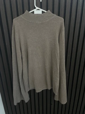 Beige stickad tröja med hög krage - En stilren beige stickad tröja med hög ribbad krage och långa ärmar. Tröjan har en rak passform och är tillverkad i ett mjukt, tunt stickat material som passar perfekt till lager på lager. Enkel och clean design utan synliga loggor eller detaljer.