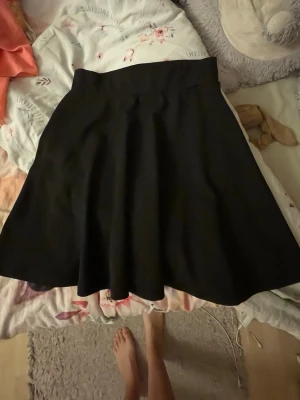 Svart vid kjol med hög midja - En svart, vid kjol med hög midja och klassisk A-linjeform. Kjolen är enkel och stilren, perfekt att matcha med olika toppar. Materialet känns mjukt och har ett fint fall.