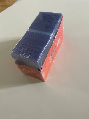 100-pack blåa kortfickor plast - Säljer ett 100-pack blåa plastfickor för kort, perfekt för att skydda samlarkort eller spelkort. Fickorna är rektangulära och levereras i en röd förpackning. Materialet är plast och de är genomskinliga med blå ton.