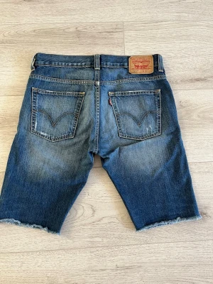 Levis 511 shorts - Säljer ett par blå jeansshorts med slitningar och råa kanter. Shortsen har fem fickor, bälteshällor och klassisk knappgylf. Perfekta för en avslappnad stil och har en cool, sliten look. Strl 33 /33
