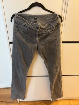 Gråa manchesterbyxor från Esprit - Snygga grå manchesterbyxor från Esprit med raka ben och klassisk femficksmodell. Byxorna har bälteshällor, knappgylf och diskret broderad logga på ena bakfickan. Perfekta för dig som gillar retrovibbar och mjukt material.