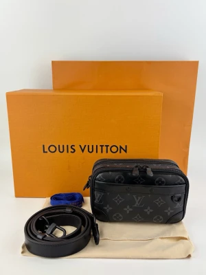 Louis Vuitton svart monogram handväska - Snygg svart handväska från Louis Vuitton i klassiskt monogrammönster. Väskan har dubbla dragkedjor, justerbar axelrem och detaljer i svart läder. Perfekt storlek för det viktigaste och en ikonisk accessoar för dig som gillar lyxig streetstyle.
