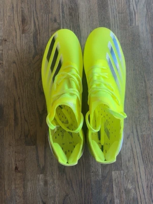 Adidas X Ghosted  - Säljer ett par riktigt snygga neongula fotbollsskor med svarta och vita detaljer på sidorna. Skorna har snörning och en modern, strömlinjeformad design som passar perfekt för snabba spelare. Ovandelen är i syntetmaterial för bra bollkontroll.
