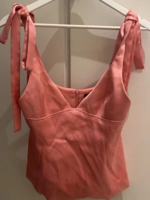 Rosa topp med knytband - Säljer denna gulliga topp med band och v-ringning. Jättefin topp som passar till flera olika sammanhang. Säljer endast eftersom att det blivit en svart sminkfläck som jag inte fått bort annars är tröjan i fint skick.💗