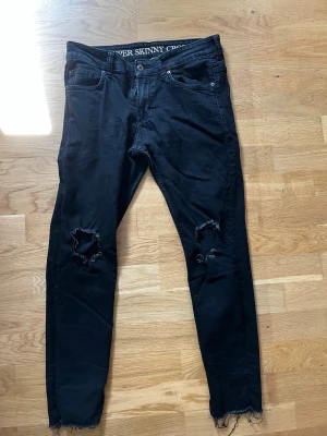Svarta skinny jeans med hål - Säljer ett par svarta super skinny jeans med slitna hål på båda knäna och råa, fransiga benslut. 