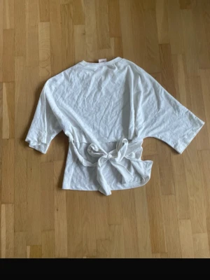 Vit topp med knyt i midjan - Säljer en enkel och stilren vit topp med knytband i midjan. Endast provad! Perfekt för en avslappnad och trendig look.