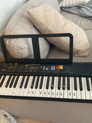 Yamaha digitalpiano med notställ - Säljer ett svart Yamaha digitalpiano med notställ. Tangenterna är märkta med bokstäver för enklare inlärning. Pianot har flera funktioner och knappar för olika ljud och rytmer. Perfekt för dig som vill lära dig spela eller öva hemma.