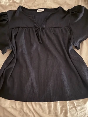 Mörkblå blus med puffärmar - Mörkblå blus från Kappahl med korta puffärmar och en rosett vid V-ringningen. Gjort av ett hyfsat tunt material.