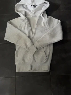 Ljusgrå zip hoodie med huva XS - Ljusgrå hoodie med dragkedja och huva. Tröjan har två fickor framtill och justerbara snören i huvan. Tillverkad i mjukt sweatshirtmaterial som är skönt mot huden. Perfekt för en avslappnad och chill stil.