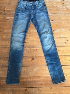 Blå slim fit jeans Anbass  - Snygga blå slim fit jeans från Anbass i klassisk denim med slitningar och ljusare partier framtill. Femficksmodell med normal midja och dragkedjegylf. Perfekta för en avslappnad och trendig look.