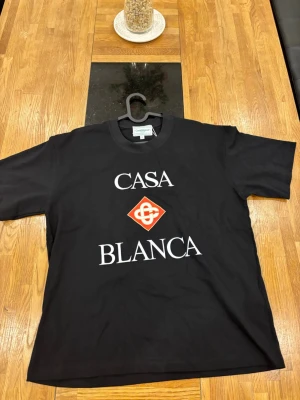 Svart Casablanca t-shirt med tryck - Snygg svart t-shirt från Casablanca med stort vitt tryck på bröstet där det står 'CASA BLANCA' och en röd logga i mitten. Klassisk passform och rund hals. Perfekt för dig som vill ha en stilren men ändå statement t-shirt.