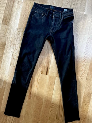 Svarta skinny jeans från Crocker - Säljer ett par svarta skinny jeans 28/32 (modell 320) från Crocker med klassisk femficksmodell. Jeansen har raka bakfickor och är tillverkade i stretchigt denimtyg för en bekväm passform.