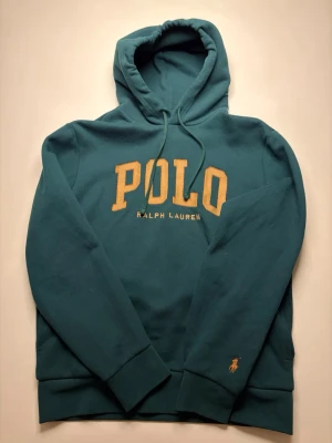 Grön hoodie från Polo Ralph Lauren - Mörkgrön hoodie med stor gul POLO-text och Ralph Lauren-brodyr på bröstet. Storlek M! Bara att höra av dig vid minsta fundering😊