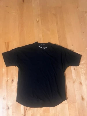 Svart Palm Angels t-shirt - Snygg svart t-shirt från Palm Angels med stort vitt logotryck på ryggen och mindre logga vid halsen fram. Klassisk passform med rund hals och korta ärmar. Perfekt för dig som gillar streetwear och vill ha en statement-piece i garderoben. L men passar M