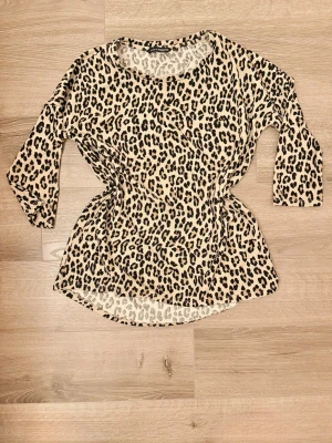 Leopardmönstrad topp från KappAhl XS - Snygg topp från KappAhl i leopardmönster med beige botten och svarta/bruna fläckar. Modellen har trekvartsärm och rund halsringning. Använt men fint skick i storlek XS.